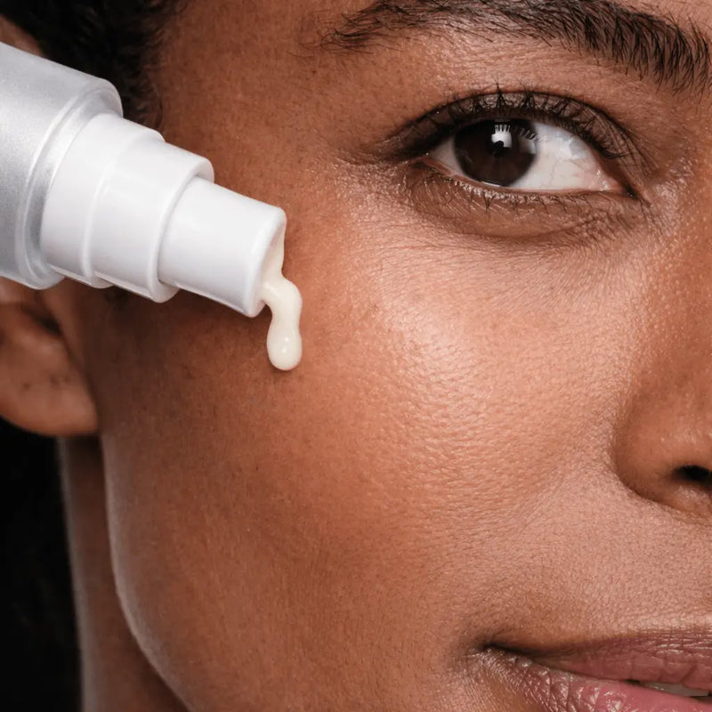 Close-up of a woman applying cream to her face with a white bottle.