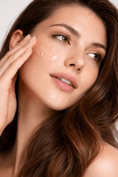 Woman applying cream to her face with a close-up of her skin.