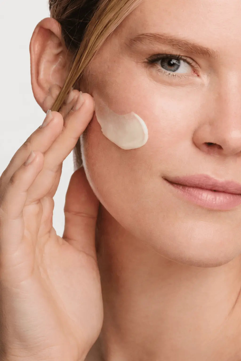 Woman applying cream to her face with a neutral background
