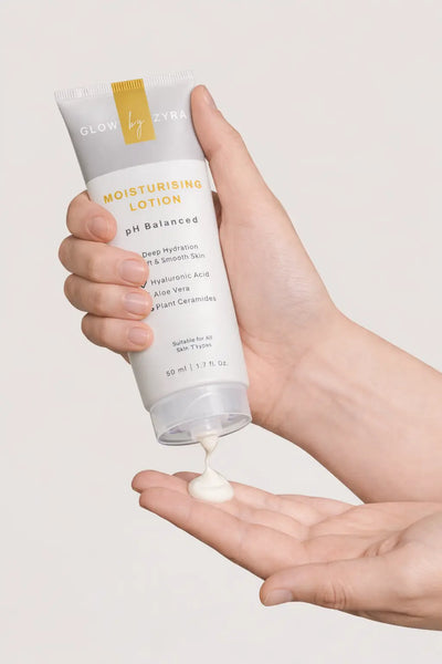 Hand holding a tube of moisturizing lotion with visible cream on the palm against a neutral background